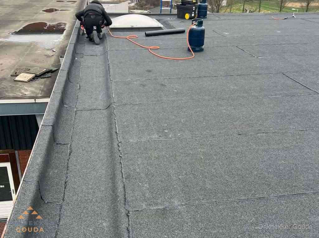 Dakdekker repareert bitumen dakbedekking op groot plat dak in Gouda